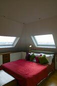 Corner of a room under a roof -- double bed with red bedspread under a skylight