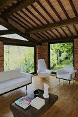 Renoviertes Landhaus mit Holzbalkendecke und hellen Sitzmöbeln vor raumhohen Fenstern