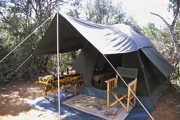 Holzstuhl mit Stoffsitzfläche und Tisch unter Vordach eines Zeltes