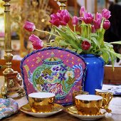 A shiny golden tea service with a tea cosy and a bunch of red tulips