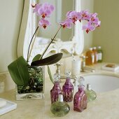 Pinkfarbene Orchidee in Glasvase und verschiedene Flakons auf dem Waschtisch