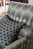 Grauer Sessel mit geschwungenem schwarzem Muster und graues Kissen mit sternförmigem schwarzen Muster