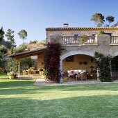 A blue sky over a finca with a plants growing up the face and a view through an archway onto a terrace