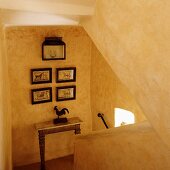 A yellow stairwell with a solid banister and a collection of pictures on a wall above a table on a half landing