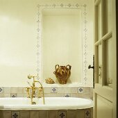 Country house bath with antique brass faucet on a bathtub and earthenware jug in a wall niche