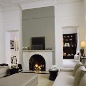 A renovated art nouveau-style living room with a grey leather sofa in front of a fireplace in a grey wall and a view of a cupboard
