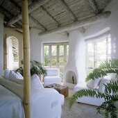 A living room with a rustic wooden ceiling in a tropical holiday home with a fireplace and a white sofa