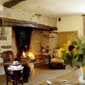 A cosy corner in a country house - a leather armchair in front of a natural stone fireplace with a fire burning in the grate