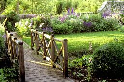A wooden bridge with a railing over a stream in a flowering garden