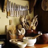 Kitchen implements in container and an assortment of knives on the wall