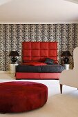 A funky bedroom - a red pouffe in front of a red bed with an upholstered headboard against an black and white wall