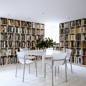 A round table in front of floor-to-ceiling book shelves on white floor boards