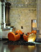 A seating area in a converted church - orange leather upholstered armchairs on a flokati rug in front of a natural stone wall