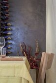 A corner in a designer restaurant - a table and chairs and a wine rack against a shiny, dark wall
