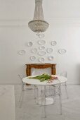An antique chandelier above a white table with transparent acrylic glass chairs on a marble floor