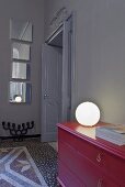A ball-shaped lamp on a red chest of drawers and an artistic mirror installation