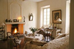 Heller Wohnraum im Landhaus mit antiken Stühlen und Tisch vor Kaminfeuer