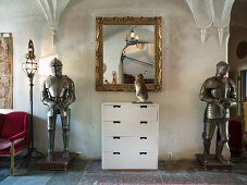 weiße Kommode mit Spiegel im Goldrahmen zwischen Ritterrüstungen im Schlossraum