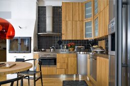 Open design kitchen with wooden door fronts and stainless steel exhaust hood in front of black wall tiles