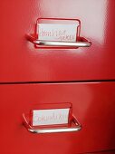 Rote Schubladen mit Metallgriffen und Beschriftung