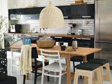 Basket pendant lamp over a dining table with chairs and wooden stools in an open plan kitchen