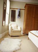 Schlafzimmer mit schlichtem Schrank aus Holz und weißem Polstersessel