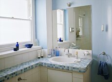 A detail of a modern blue bathroom with a washbasin set in a unit with mosaic tiled top, mirror