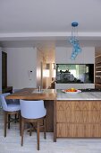 Blue bar stools at island unit breakfast bar with wooden drawers in contemporary kitchen