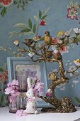 A candelabra, animal figurines and glasses against a wall with floral patterned wallpaper