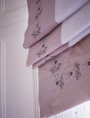 A detail of a neutral embroidered roman blind