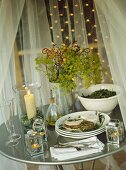 Metal table, draped with white sheer curtain, set for meal in gazebo.