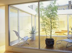 Blick durch Fenster auf Terrasse mit Holzboden und modernen Gartenstühlen