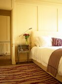 Schlafzimmer mit weiss getäfelten Wänden und gestreiftem Teppichläufer neben Bett
