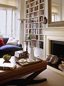 A detail of a traditional sitting room with fireplace, upholstered table, built in book shelves