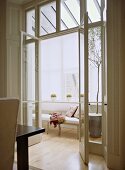 View through open French doors to a modern conservatory sitting room, upholstered sofa, wood floor