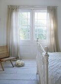 White room with Victorian frame bed and wooden chair and ostrich eggs in window.