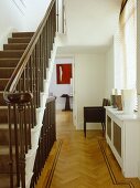 A traditional neutral hallway with parquet wood floor, staircase with view through open door beyond