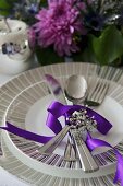 A place setting with cutlery and a purple ribbon in front of a bunch of flowers