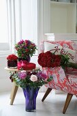 Various bunches of flowers in coloured glass vases next to a 1950s style armchair
