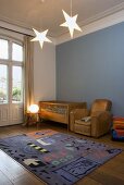 A child's room in a country house with a blue wall and a cot, a leather armchair and a rug