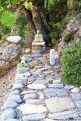 Mit Natursteinen ausgelegter Weg führt zur Buddha-Statue im Garten