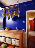 Küchenmöbel mit Schneideblock und Kochgeschirr am Regal hängend vor blauer Wand