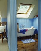Blick durch offene Tür in blaues holzvertäfeltes Bad mit Dachfenster über freistehender Badewanne im Vintagelook