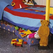 Bett mit rot und blau gestreifter Bettdecke, darunter Schubladen mit Spielzeug