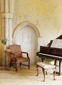 Wohnzimmer in einem Landhaus mit gotischem Steinpfeiler und gotischer Tür, daneben ein Sessel und ein Flügel
