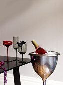 A bottle of rose champagne in a champagne chiller with glasses on a black table
