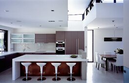 Open-plan living with a white counter and bar stools in a kitchen with a designer dining area
