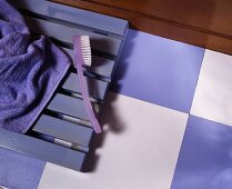 Violette Zahnbürste auf violettem Holzrost und auf Boden mit Schachbrettmuster