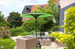 Wicker furniture under a green sunshade on a terrace in front of a house