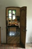 Blick durch antike, offene Holztür auf gedeckten Tisch und schwarzweissen Fliesenboden in französischer Landhausküche